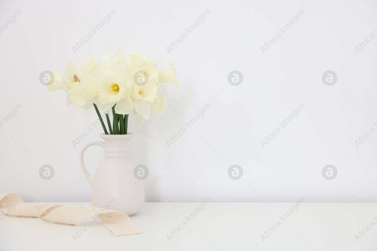 Beautiful daffodils in vase on white table at home, space for text Photo of Beautiful daffodils in vase on white table at home, space for text