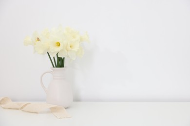 Photo of Beautiful daffodils in vase on white table at home, space for text