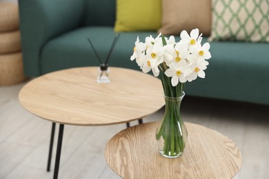 Photo of Beautiful daffodils in vase on wooden nesting table at home