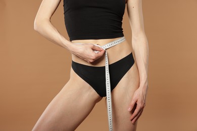 Photo of Woman with slim body and measuring tape on beige background, closeup