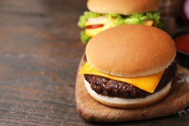 Photo of Tasty cheeseburgers on wooden table, closeup. Space for text