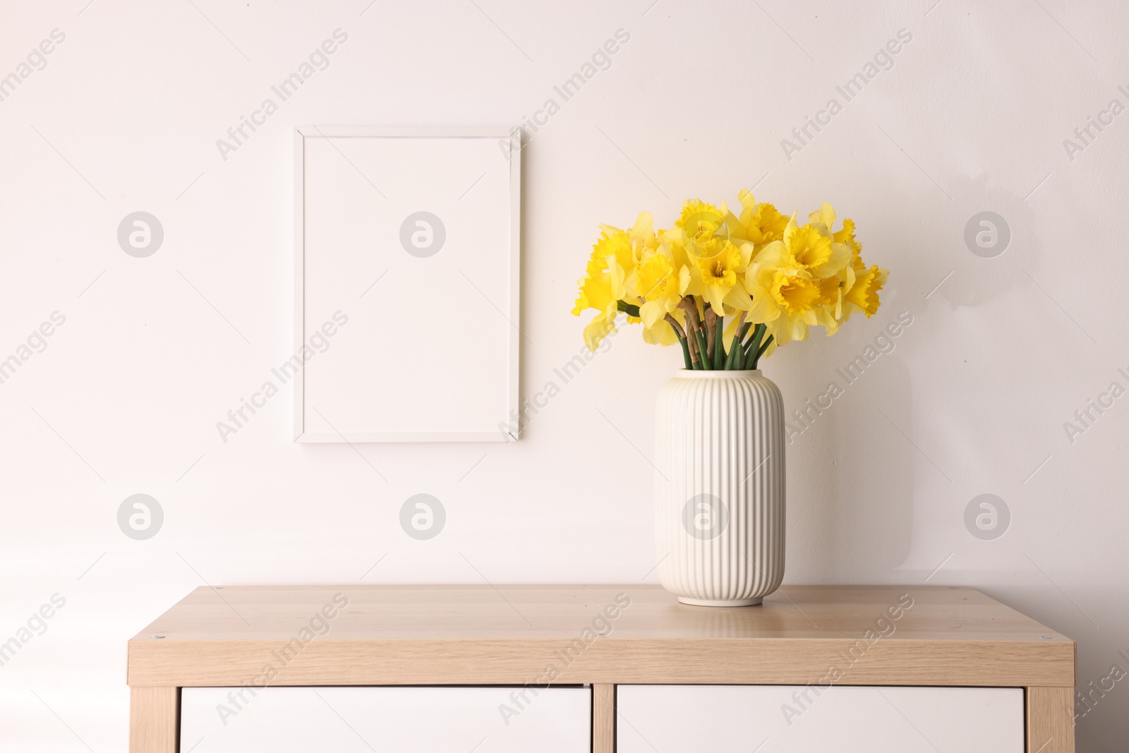 Beautiful daffodils in vase and picture frame on cabinet at home Photo of Beautiful daffodils in vase and picture frame on cabinet at home