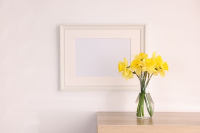 Photo of Beautiful daffodils in vase and picture frame on cabinet at home