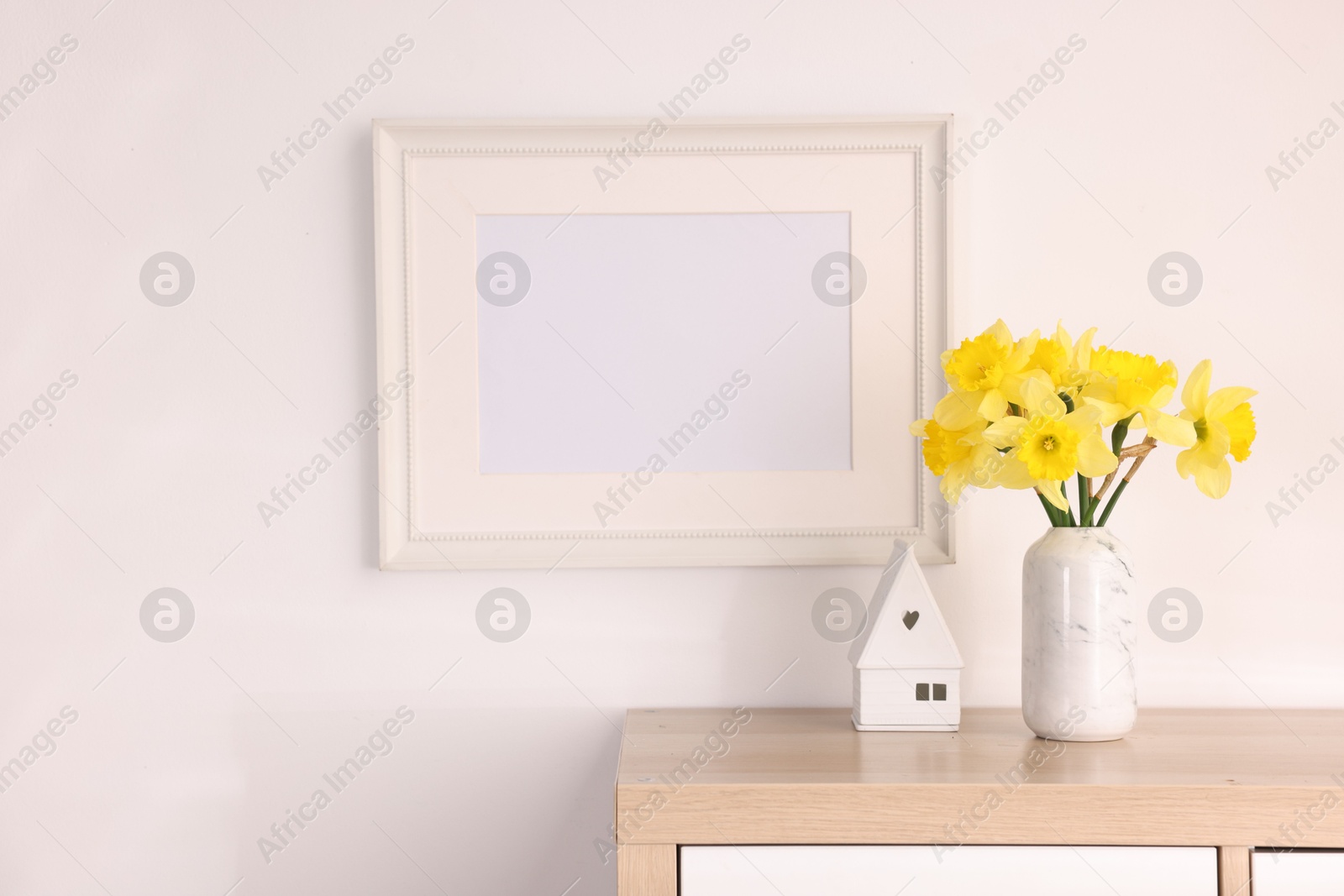 Beautiful daffodils in vase, stylish home decor and picture frame on cabinet in room Photo of Beautiful daffodils in vase, stylish home decor and picture frame on cabinet in room