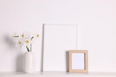 Photo of Beautiful daffodils in vase and picture frames on white table at home