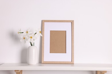 Photo of Beautiful daffodils in vase and picture frame on white table at home