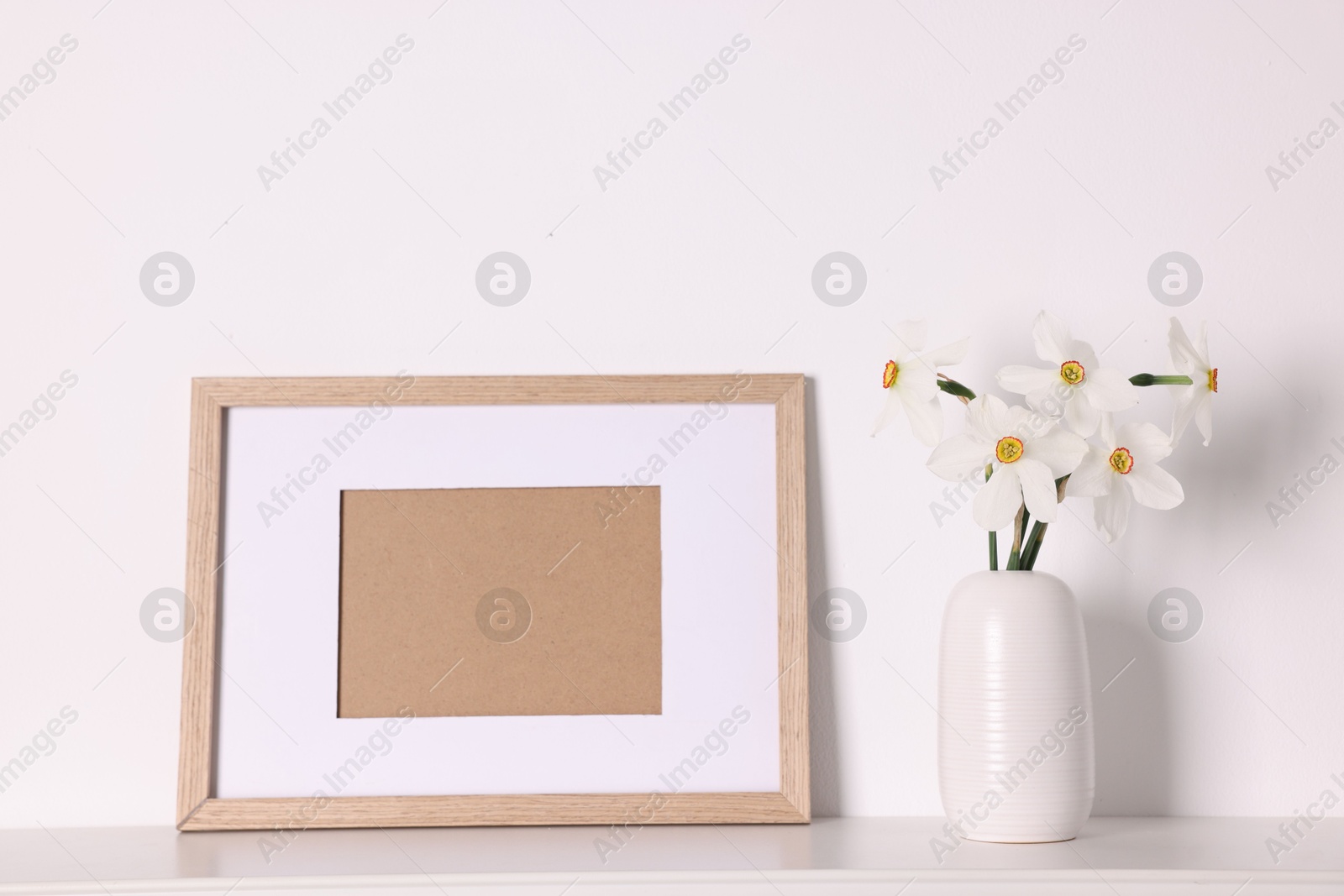 Beautiful daffodils in vase and picture frame on white table at home Photo of Beautiful daffodils in vase and picture frame on white table at home