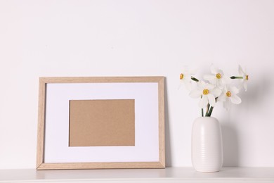 Photo of Beautiful daffodils in vase and picture frame on white table at home