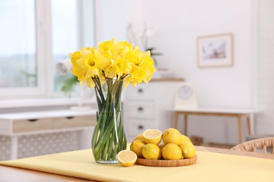 Photo of Beautiful daffodils in vase and lemons on wooden table at home