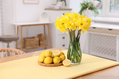 Photo of Beautiful daffodils in vase and lemons on wooden table at home