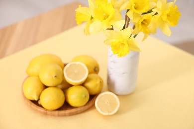 Photo of Beautiful daffodils in vase and lemons on table at home, closeup