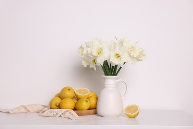 Photo of Beautiful daffodils in vase and lemons on white wooden table