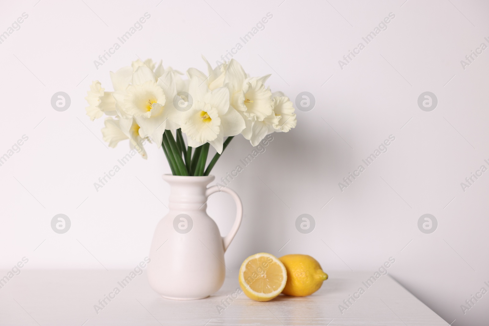 Beautiful daffodils in vase and lemons on white wooden table Photo of Beautiful daffodils in vase and lemons on white wooden table
