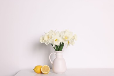 Photo of Beautiful daffodils in vase and lemons on white wooden table