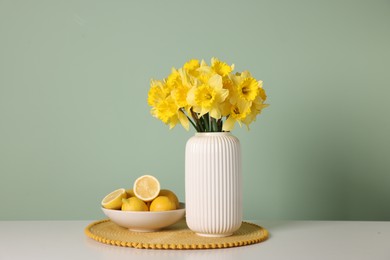 Photo of Beautiful daffodils in vase and lemons on white table near light green wall