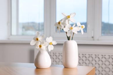 Photo of Beautiful daffodils in vases on wooden table at home