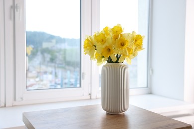 Photo of Beautiful daffodils in vase on wooden table at home. Space for text