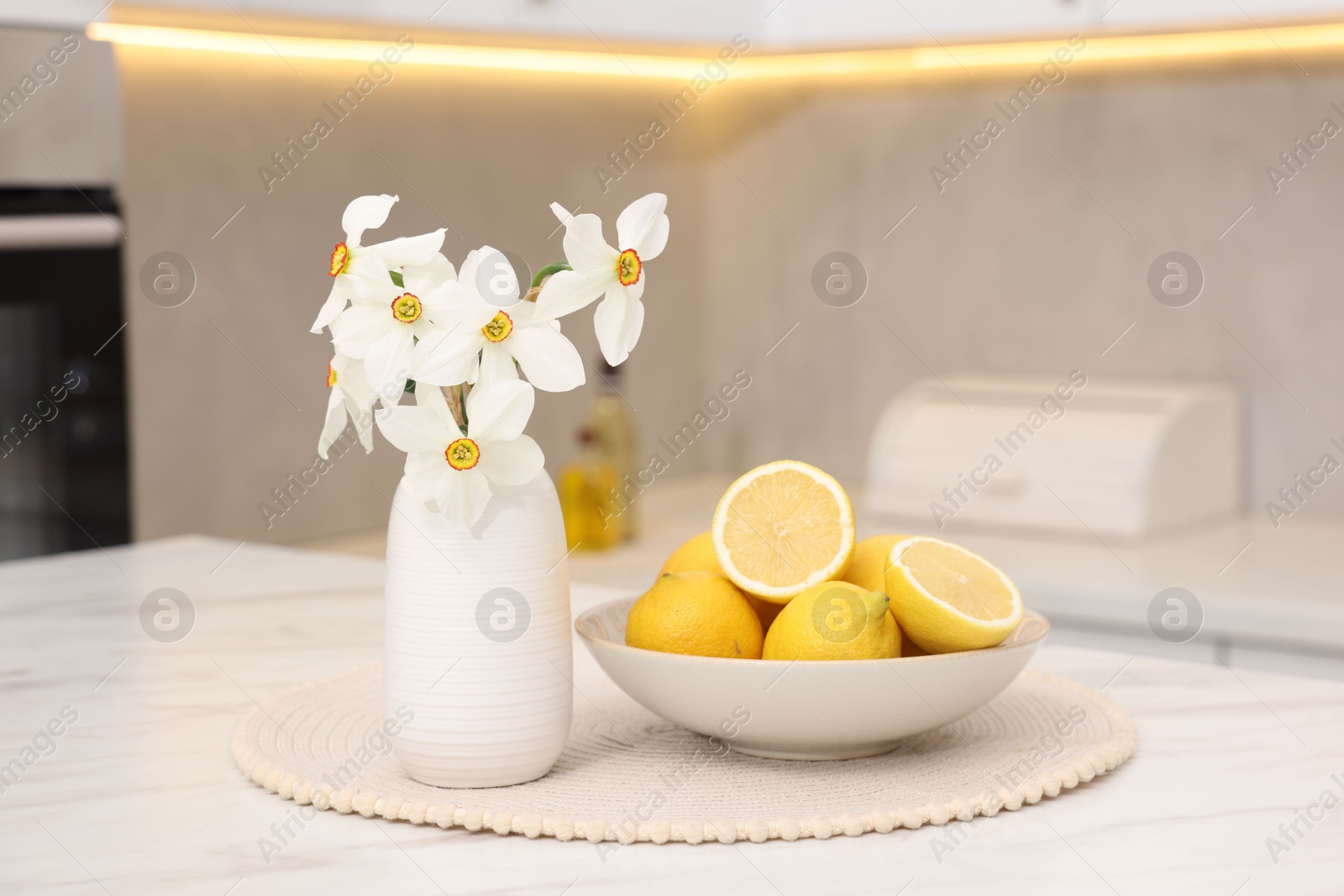 Beautiful daffodils in vase and lemons on white marble table in kitchen Photo of Beautiful daffodils in vase and lemons on white marble table in kitchen