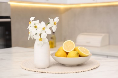 Photo of Beautiful daffodils in vase and lemons on white marble table in kitchen