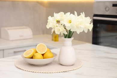 Photo of Beautiful daffodils in vase and lemons on white marble table in kitchen