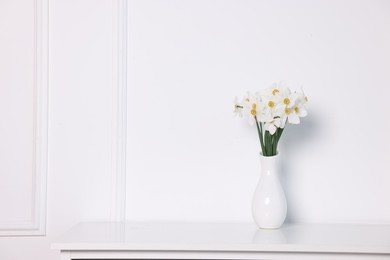Photo of Beautiful daffodils in vase on cabinet near white wall at home. Space for text