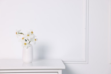 Photo of Beautiful daffodils in vase on cabinet near white wall at home. Space for text