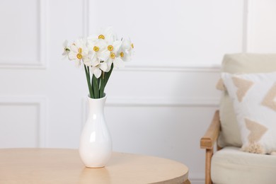 Photo of Beautiful daffodils in vase on wooden table at home. Space for text