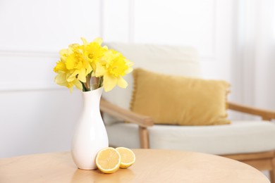 Photo of Beautiful daffodils in vase and lemons on wooden table at home. Space for text