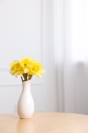 Photo of Beautiful daffodils in vase on wooden table at home. Space for text