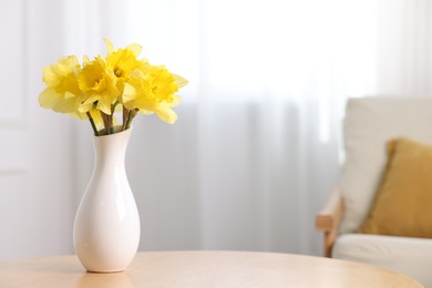 Photo of Beautiful daffodils in vase on wooden table at home. Space for text