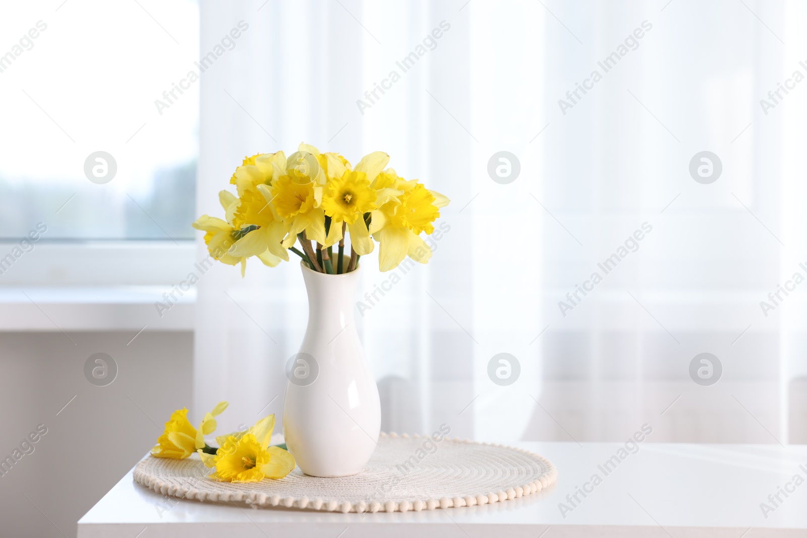 Beautiful daffodils in vase on white table at home. Space for text Photo of Beautiful daffodils in vase on white table at home. Space for text