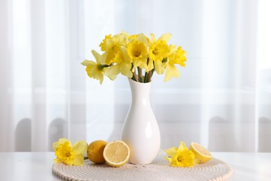 Photo of Beautiful daffodils in vase and lemons on white table at home