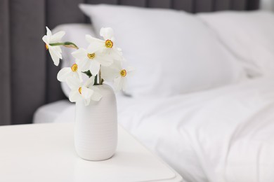Photo of Beautiful daffodils in vase on white table near bed at home. Space for text