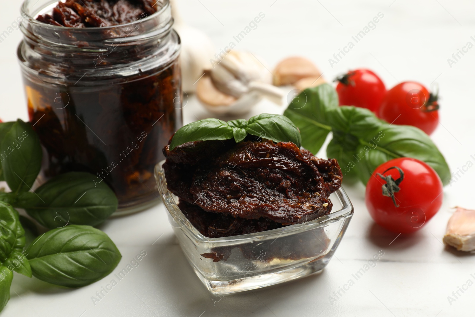 Delicious sun dried tomatoes, fresh vegetables, basil and garlic on white table, closeup Photo of Delicious sun dried tomatoes, fresh vegetables, basil and garlic on white table, closeup