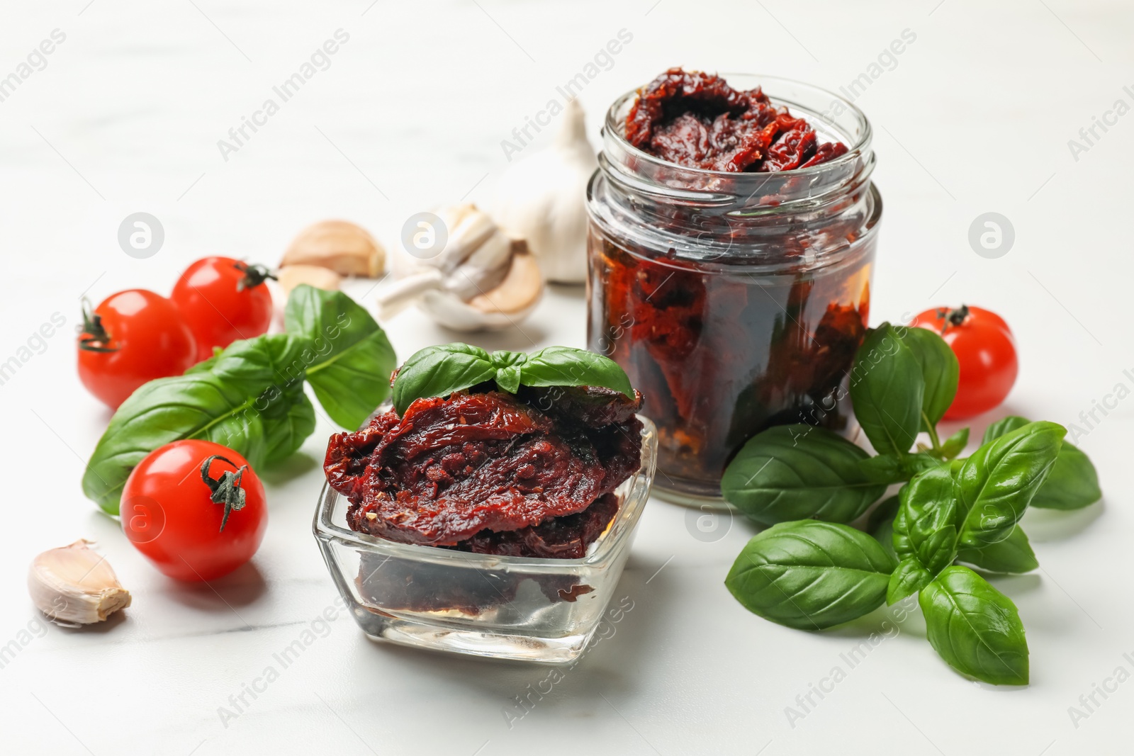 Delicious sun dried tomatoes, fresh vegetables, basil and garlic on white table, closeup Photo of Delicious sun dried tomatoes, fresh vegetables, basil and garlic on white table, closeup