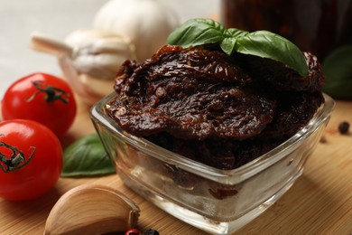 Photo of Delicious sun dried tomatoes, fresh vegetables, basil and garlic on wooden table, closeup