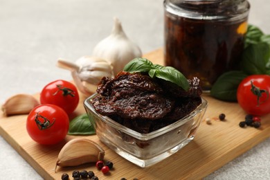 Photo of Delicious sun dried tomatoes, fresh vegetables, basil and garlic on light grey table, closeup