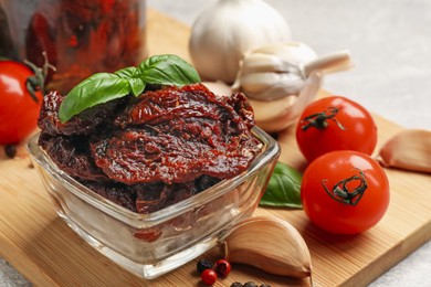 Photo of Delicious sun dried tomatoes, fresh vegetables, basil and garlic on light grey table, closeup