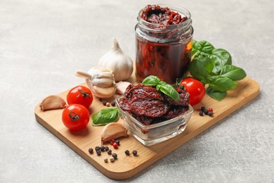 Photo of Delicious sun dried tomatoes, fresh vegetables, basil and garlic on light grey table