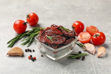 Photo of Delicious sun dried tomatoes, fresh vegetables, rosemary and garlic on light grey table