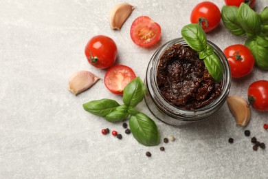 Photo of Delicious sun dried tomatoes, fresh vegetables, basil and garlic on light grey table, flat lay