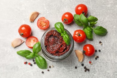 Photo of Delicious sun dried tomatoes, fresh vegetables, basil and garlic on light grey table, flat lay
