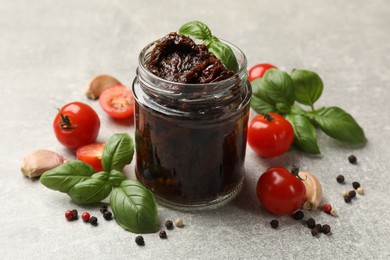 Photo of Delicious sun dried tomatoes, fresh vegetables, basil and garlic on light grey table, closeup
