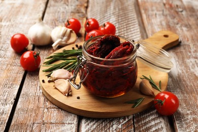 Photo of Delicious sun dried tomatoes, fresh vegetables, rosemary and garlic on wooden table, closeup