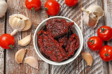 Photo of Delicious sun dried tomatoes, fresh vegetables and garlic on wooden table, flat lay