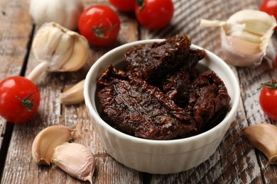 Photo of Delicious sun dried tomatoes, fresh vegetables and garlic on wooden table, closeup