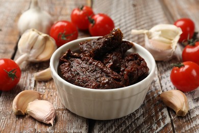 Photo of Delicious sun dried tomatoes, fresh vegetables and garlic on wooden table, closeup