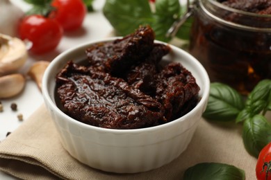 Photo of Delicious sun dried tomatoes, fresh vegetables, basil and garlic on white table, closeup