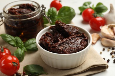 Photo of Delicious sun dried tomatoes, fresh vegetables, basil and garlic on white table, closeup