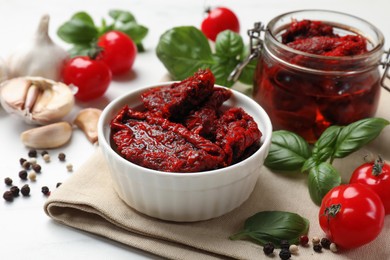 Photo of Delicious sun dried tomatoes, fresh vegetables, basil and garlic on white table, closeup